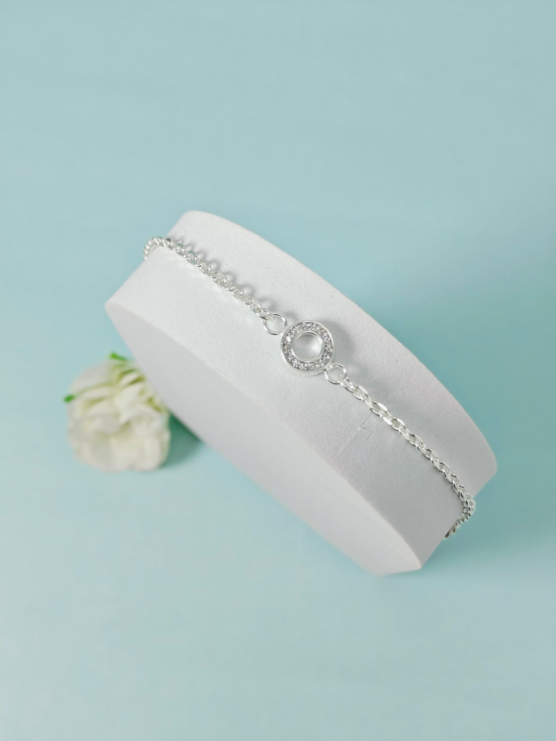 Silver bracelet with a central gemstone on a white cushion against a light blue background